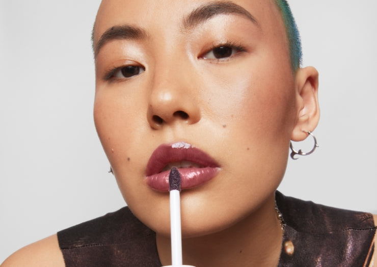 Model applies Milk Makeup Odyssey Lip Oil Gloss in Voyage to lips on a white background.