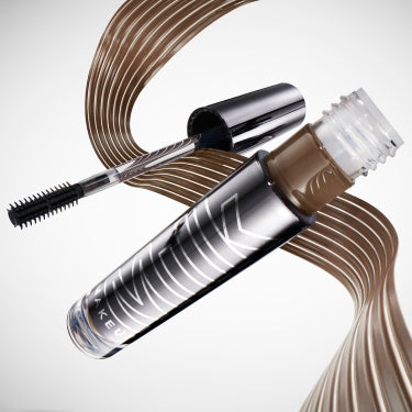 Flying tube of Milk Makeup KUSH High Roll Brow Tint with a swipe behind it on a white background.