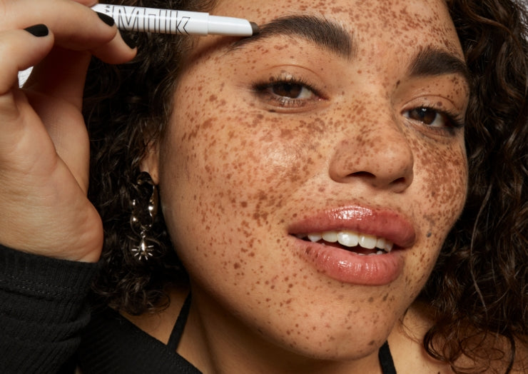 Model wears Milk Makeup KUSH Brow Shadow Stick on white background