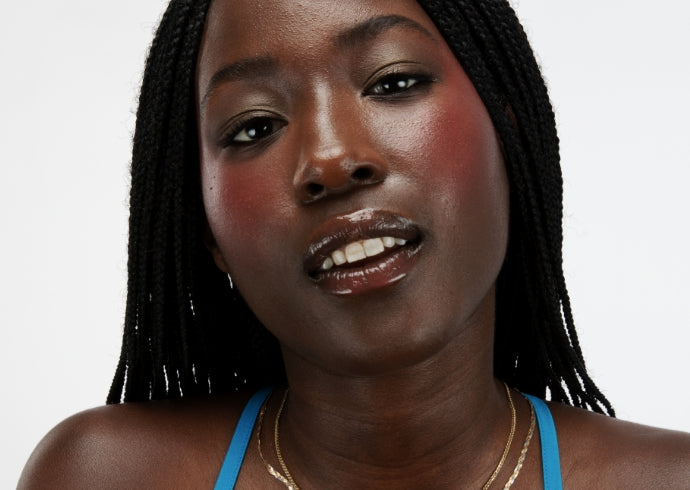 Portrait of a model with box braids wearing Milk Makeup Bionic Blush in Beyond on a white background.