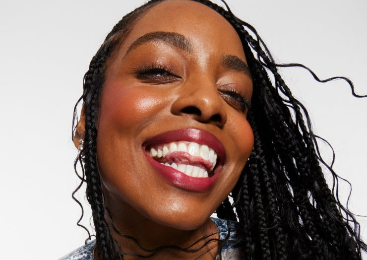 Smiling model wears a full face of Milk Makeup Products, including Hydro Grip Set + Refresh Spray against a light gray background