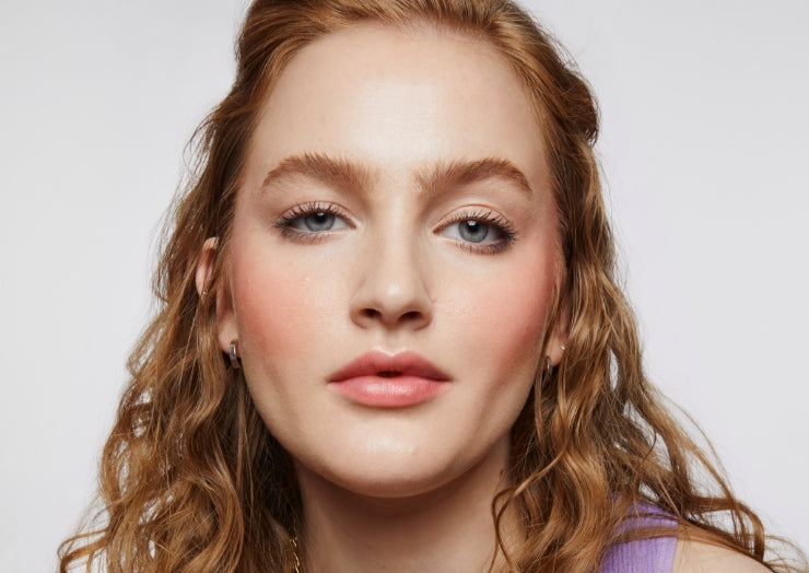 Model with wavy strawberry blonde hair wears a full face of Milk Makeup products on a white background