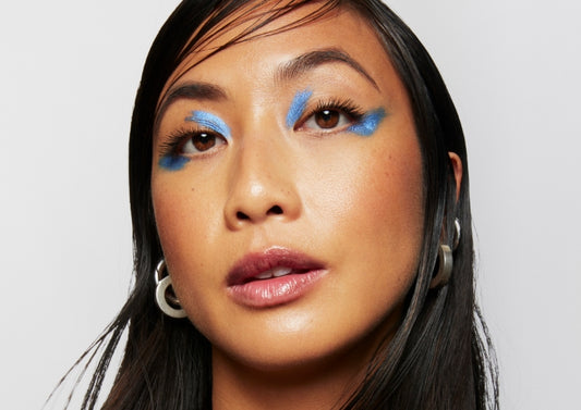 Model wears a full face of Milk Makeup with blue graphic eyeshadow on a white background