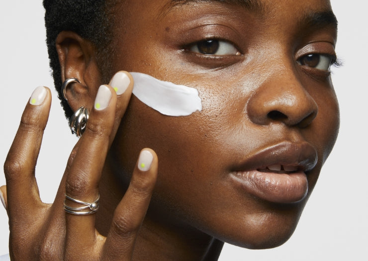 Model applies swipe of Milk Makeup Vegan Milk Moisturizer to her face on a white background