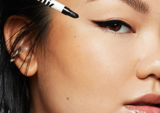 Model wears a cat eye wing drawn with Milk Makeup Infinity Long Wear Eyeliner in Outer Space on a white background. The wing is smudged out.