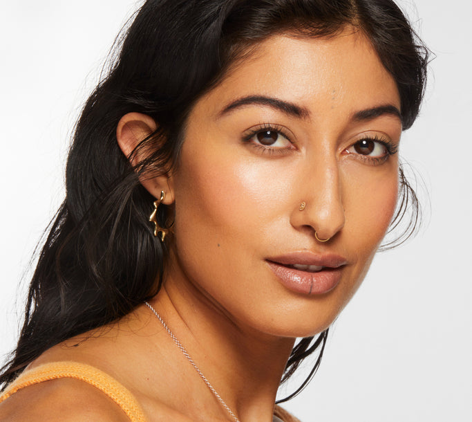 Model against a white background wears no-makeup makeup achieved with Milk Makeup Cloud Glow Priming Foam