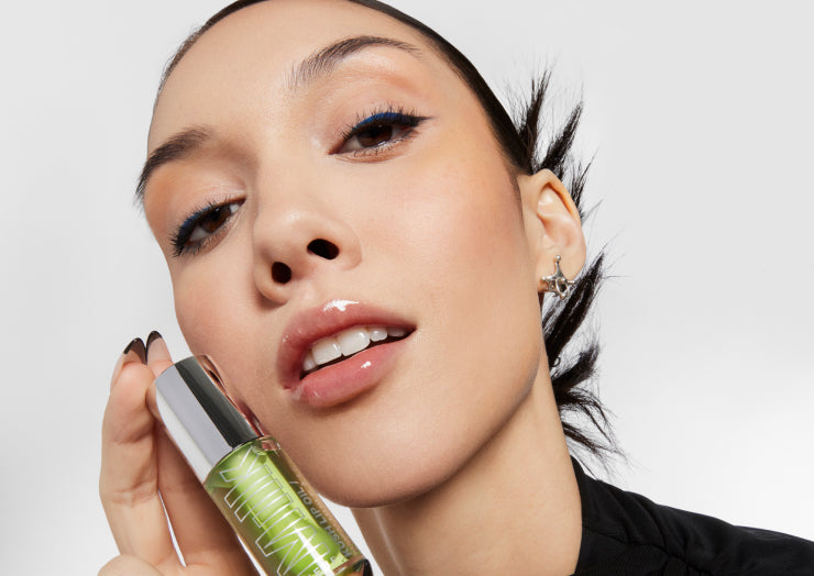  Model holds a tube of KUSH Lip Oil in Green Dragon up to her face against a white background 