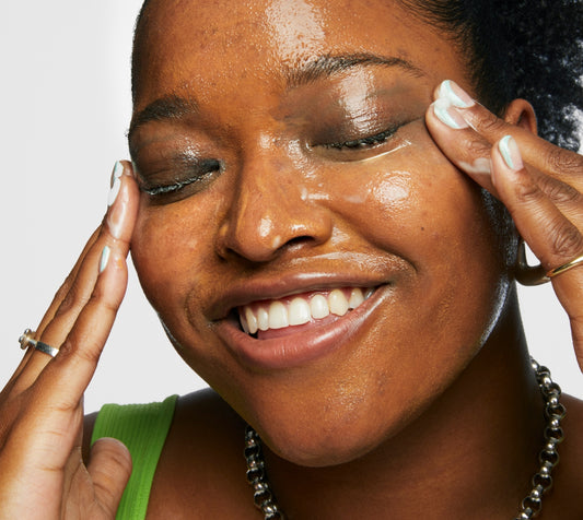 Model uses Milk Makeup Hydro Ungrip Cleansing Balm to remove makeup from her face against a white background.