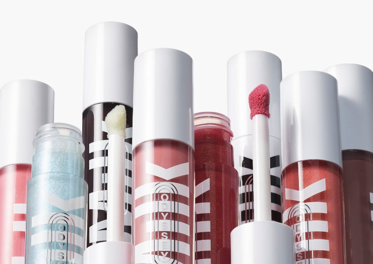 Artistic product shot of several bottles of Milk Makeup Odyssey Lip Oil Gloss on a white background