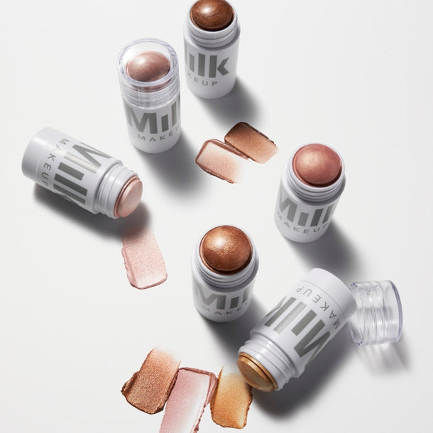 Overhead shot of Milk Makeup Highlighter sticks in shades Spark (golden copper), Flare (rose gold), and Strobe (gold) next to their swatches on a white background.
